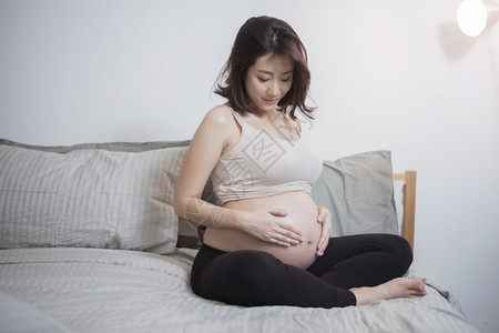 美丽的亚洲孕妇坐在床上抚摸肚子图片