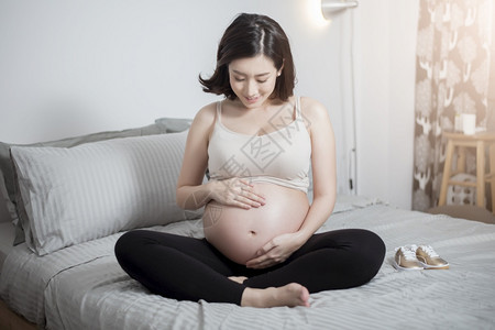 美丽的亚洲孕妇坐在床上抚摸肚子图片