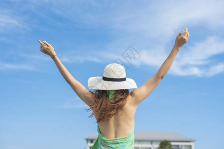 带着白帽子的女旅行者背面正在海滩和蓝天空上放松图片