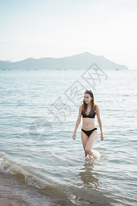 穿黑色比基尼的漂亮女人正在海上走夏天的概念图片