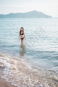 穿黑色比基尼的漂亮女人正在海上走夏天的概念图片