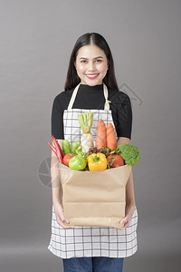美丽的年轻女肖像蔬菜在杂货袋里灰色背景的工作室图片
