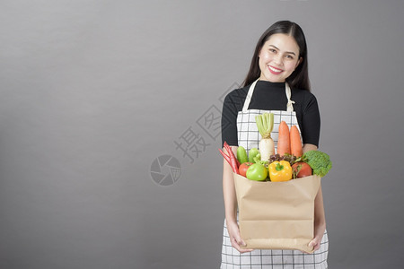 美丽的年轻女肖像蔬菜在杂货袋里灰色背景的工作室图片