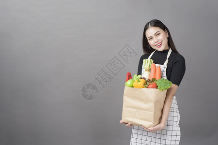 美丽的年轻女肖像蔬菜在杂货袋里灰色背景的工作室图片