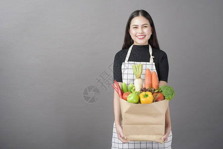 美丽的年轻女肖像蔬菜在杂货袋里灰色背景的工作室图片