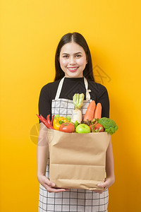 美丽的年轻女士拿着蔬菜在杂货袋黄色背景工作室黄色背景图片