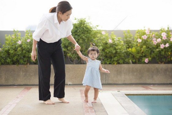 亚洲母亲牵着她的女婴手走出游泳池家庭父母安全概念亚洲母亲牵着她的女婴手走出游泳池家庭安全概念图片