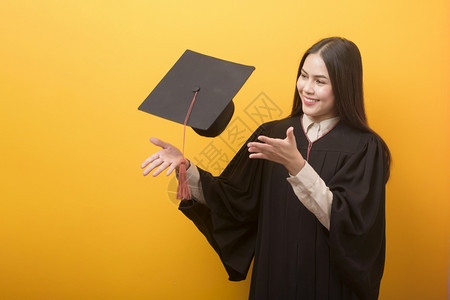 在黄色背景下穿着毕业礼服的快乐女人图片