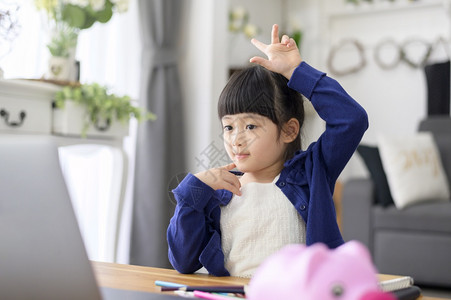 一个可爱的小女孩正在使用笔记本电脑在家中通过互联网在线学习图片