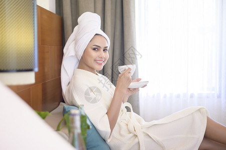 一个穿着白浴袍和毛巾的放松妇女早上喝咖啡图片