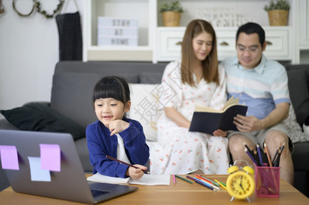 亚洲快乐的女儿正在使用笔记本电脑通过互联网在线学习而父母却坐在家中沙发上图片