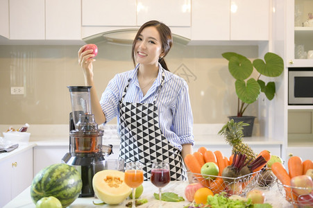 一位美丽的女士正在准备健康的新鲜果汁而厨房的餐桌上蔬菜和果汁健康概念图片