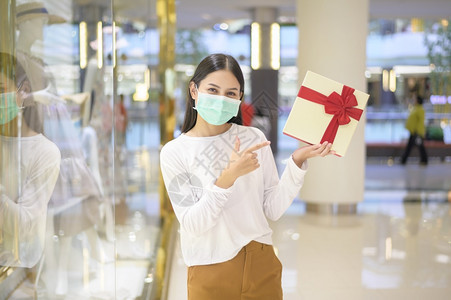 身着保护面罩的妇女在购物中心持有礼品箱在新冠大流行病感恩节和圣诞概念下购物身着保护面罩的妇女在购物中心持有礼品箱身着新冠大流行病图片