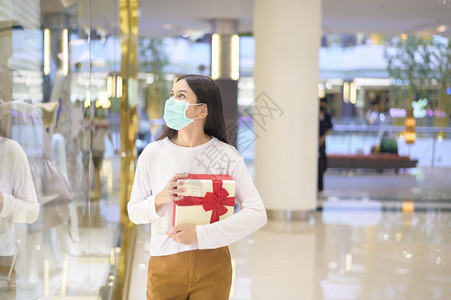 身着保护面罩的妇女在购物中心持有礼品箱在新冠大流行病感恩节和圣诞概念下购物身着保护面罩的妇女在购物中心持有礼品箱身着新冠大流行病图片