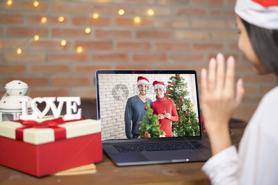 一位戴着红色圣诞老人帽子的微笑年轻女在圣诞节当天与家人和朋友在社交网络上进行视频通话图片