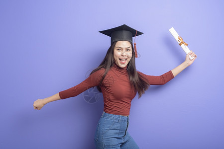 具有紫背景毕业上限的年轻大学女生的肖像图片