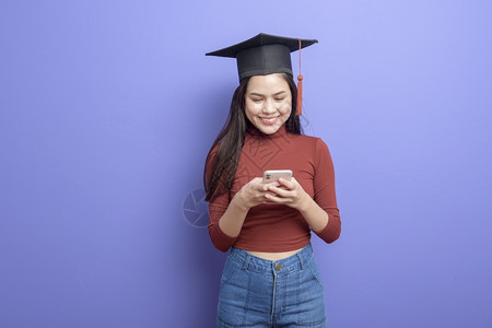 具有紫背景毕业上限的年轻大学女生的肖像图片