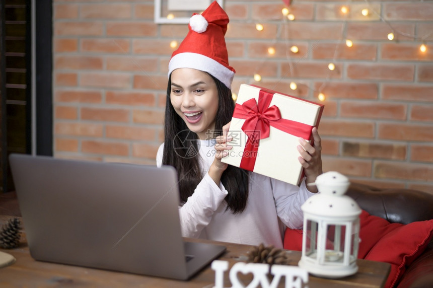 一位戴着红色圣诞老人帽子的微笑年轻女在圣诞节当天与家人和朋友在社交网络上进行视频通话图片