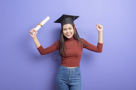 具有紫背景毕业上限的年轻大学女生的肖像图片