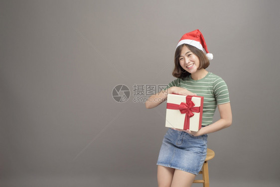 穿着红色圣诞老人帽子的漂亮女肖像她拿着礼物盒超过工作室背景圣诞节和新年概念穿着红色圣诞老人帽子的漂亮女肖像超过工作室背景圣诞节和图片