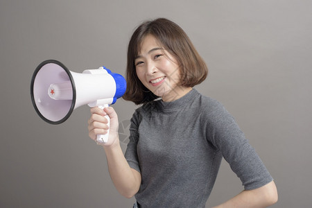 年轻美丽的亚洲女在演播室背景上拿着扩音器的肖像图片