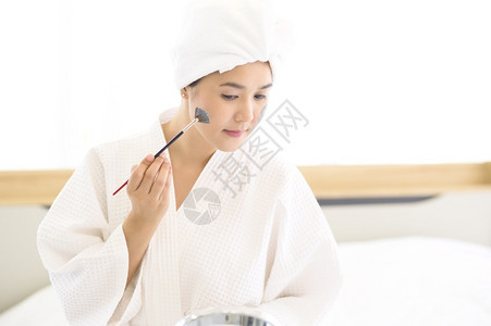 穿着白浴袍的快乐美丽妇女运用面罩皮肤护理和治疗概念图片