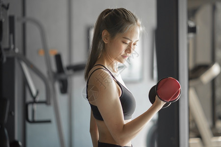 一名在体育场上穿着哑铃运动的美丽年轻女子健康生活方式体育培训健康体育的概念一名在体育场上穿着哑铃运动的美丽年轻女子健康生活方式和图片