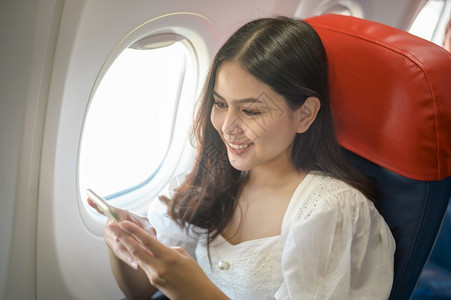 美丽的女旅行者在飞机上使用智能手机图片