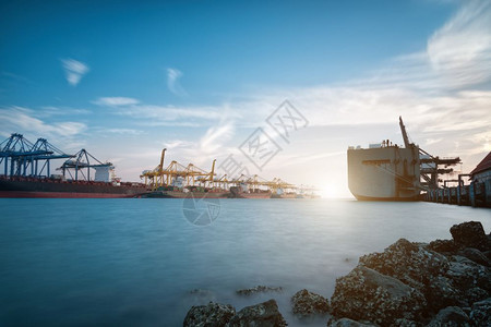 日出时载起重机和蓝天空在海上航行的商港口货船图片