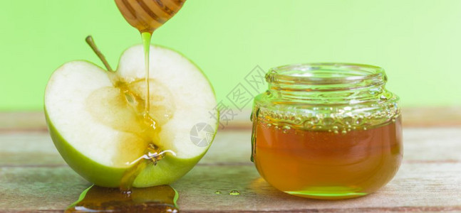 犹太节日苹果罗什哈沙纳在照片上有蜂蜜在罐子里滴在绿色背景木绿色苹果蜂蜜图片