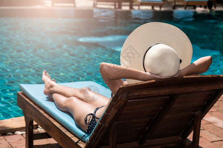 戴大帽子的亚洲女青年在游泳池边的蓝水中晒日光浴图片