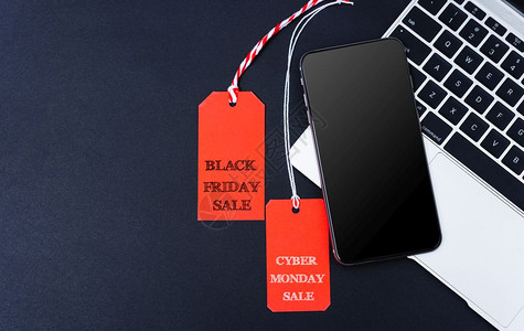 网上购物络周一销售文本和黑色星期五销售文本同时贴在智能手机和黑背景笔记本电脑的红色标签上图片