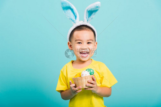 亚洲可爱的小孩男微笑身穿兔子耳朵和黄色T恤衫站着拿篮子图片