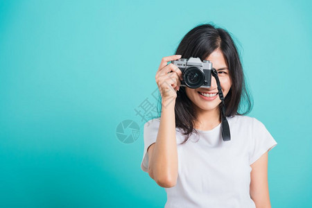 旅游者快乐的亚洲美丽年轻女穿着夏帽微笑拿无照相机站在无的夏帽拍摄蓝背景影棚的照片复制文本空间图片