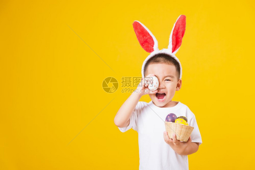 肖像快乐的亚洲可爱的小男孩微笑着站着如此快乐穿着白色T恤和兔子耳朵在复活节那天拿着复活节彩蛋摄影棚拍摄黄色背景和复制空间图片