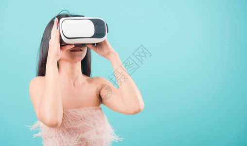 亚洲快乐的肖像美丽年轻女站在她的微笑中使用虚拟现实头戴耳机在蓝色背景的VR眼镜设备上玩复制文本空间图片