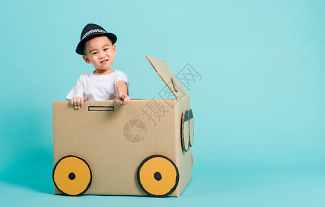 快乐的亚洲儿童男孩在驾驶车时微笑由纸箱想象力暑假旅行概念蓝背景摄影棚拍图片