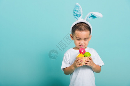 亚洲可爱的小孩男微笑带着兔子耳朵和白色T恤衫站在篮子上着图片