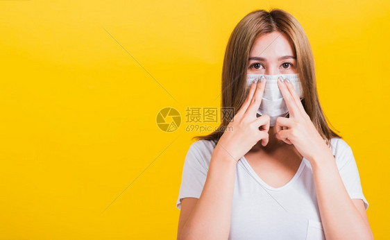 身戴面罩的亚洲美貌年轻肖像女脸罩保护过滤尘pm25防污染烟雾COVID和空气污染她使用黄色背景的手桥鼻子并有复制空间图片