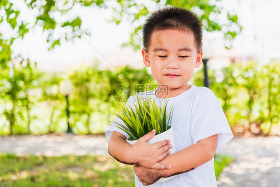 世界环境日与拯救世界概念亚洲可爱的快乐小男孩手在绿色花园背景下在白锅上抓着小树图片