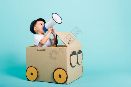 快乐的亚洲儿童男孩笑在驾驶汽车上由纸板盒想象力制作有扩音器暑假旅行概念蓝背景摄影棚拍复制文本空间图片