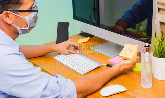 身戴保护面罩及消毒凝胶的亚洲青年商人在家中办公室用电脑工作图片