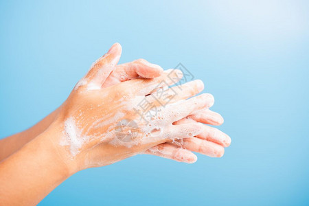 肥皂泡沫亚洲青年妇女用肥皂洗手时有泡沫卫生预防COVID19或冠状保护概念蓝底隔离背景