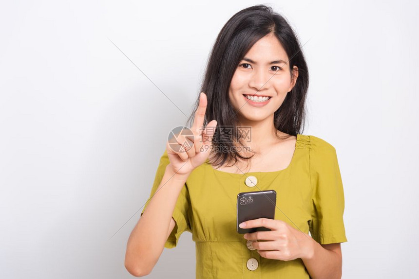 透过手机智能保持微笑展示她的手指触摸着一些寻找相机的东西拍摄照片在白色背景的摄影棚中拍图片