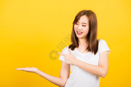 亚洲快乐肖像美丽可爱的年轻女孩站着穿T恤手持掌上的东西图片