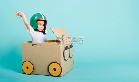 快乐的亚洲儿童男孩在驾驶汽车时笑着Helmet的Helmet亚洲男孩由纸板盒想象力暑假旅行概念蓝背景摄影棚拍复制文本空间图片