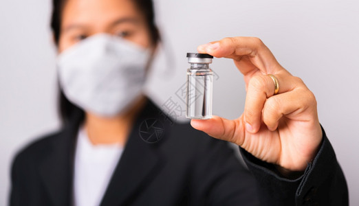 身穿外科保护布面罩的亚洲女医生面戴罩防止冠状她持有的氨水瓶疫苗侧重于玻璃透明工作室拍摄孤立的白色背景COVID19概念图片