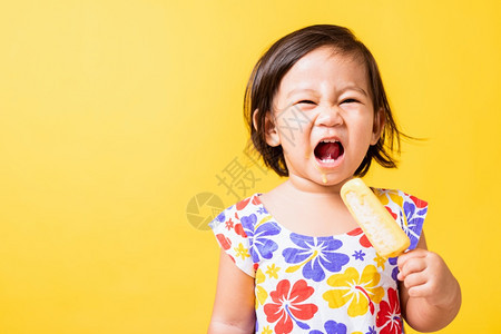 快乐的亚洲小婴儿或孩可爱的女快乐肖像笑有吸引力的小女孩笑穿着鸡样衬衫并吃甜木冰淇淋摄影棚拍着黄色背景夏季概念图片