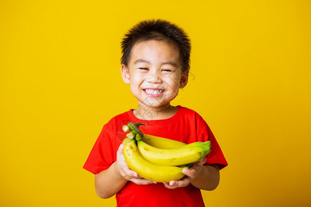 带着红色T恤的笑脸拿着香蕉梳子果拍摄室以黄色背景隔离图片