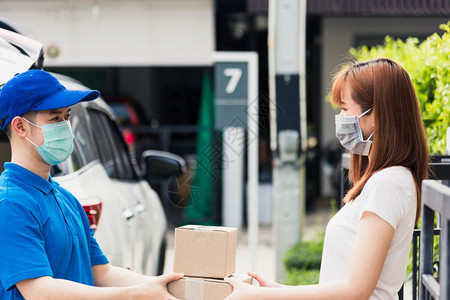 亚洲青年送货员在线购买亚洲青年快递员提供包邮箱他保护面罩服务在宵禁检疫大流行冠状COVID19下在前家接受包箱的女客户图片